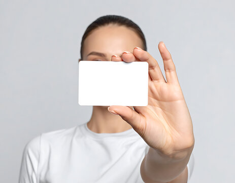 Woman holding blank white card in front of face, presenting space for text or logo, neutral background