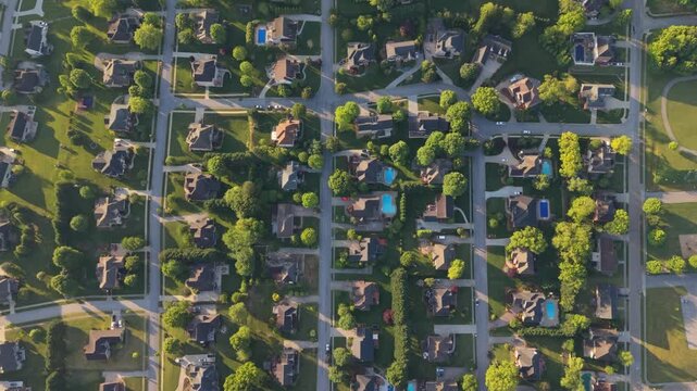 Aerial perspective of a suburban area in Johnson City, Tennessee, highlighting residential houses with well-maintained lawns, swimming pools, and tree-lined streets illuminated by sunlight