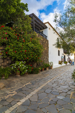 View of the historic cobblestone streets and white buildings adorned with vibrant red flowers and lush greenery in Betancuria, Canary Islands, Spain.