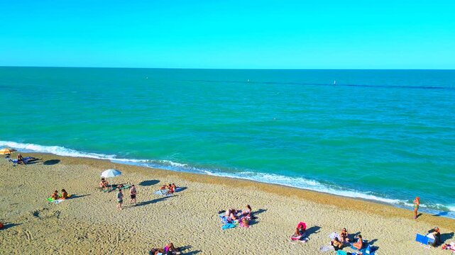 PORTO RECANATI, ITALY - JULY 30, 2025: Aerial push-in shot from the beach. Bathers and walkers enjoy the sandy beach, lying with colored parasols and loungers in front of pristine Adriatic Sea waters