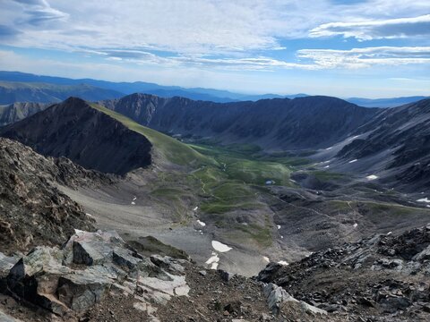 View of the Grays and Torreys Summer Trailhead area featuring rugged mountain peaks, rocky slopes, patches of snow, and a green valley in Silver Plume, Colorado, United States.