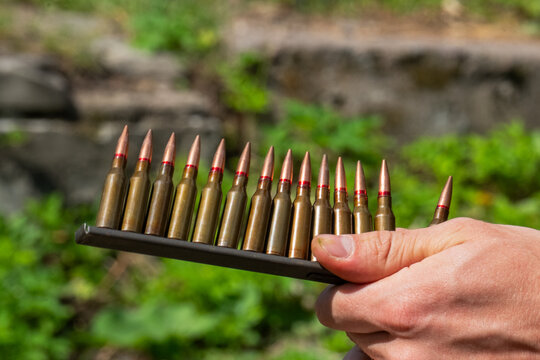Hand holding vintage steel ammunition stripper clip with rifle bullets row target shooting view.
