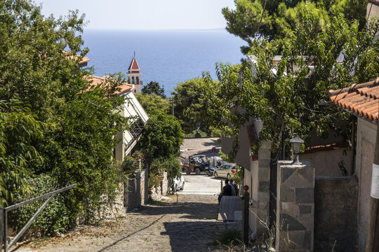 View of a stone-paved street leading towards a historic church bell tower with the sea in the background in Zakinthos, Greece.