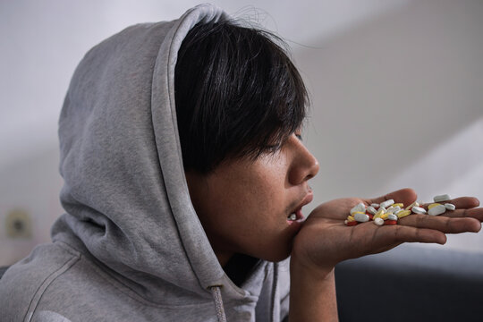 Young man in Grey Hoodie Taking Handful of Pills, Depicting Drug Overdose and Addiction