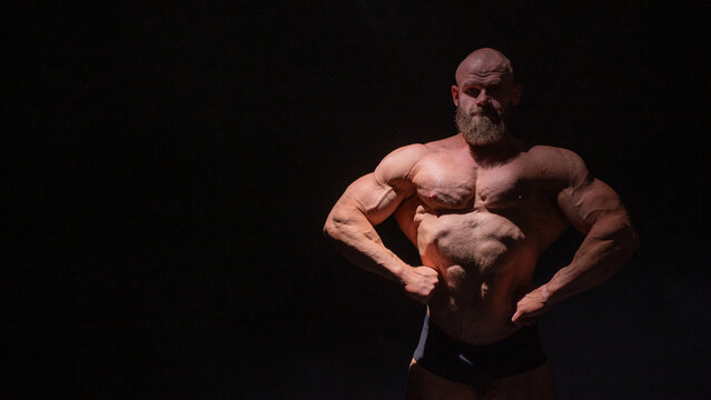 A male bodybuilder poses in shorts, showing off his muscles.