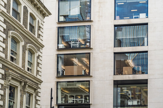 View of the modern glass facade of an office building adjacent to a historic brick structure near Liverpool Street in London, England, United Kingdom.