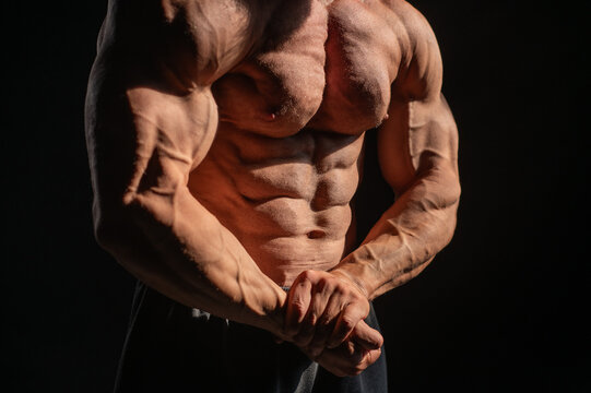 A male bodybuilder poses in shorts, showing off his muscles. Close-up of his chest and abs.