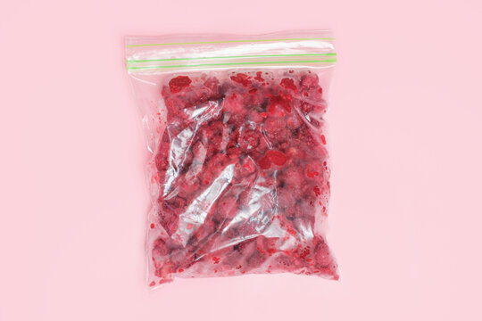 Raspberry berry in cellophane zip-lock bags on pink background close-up top view.