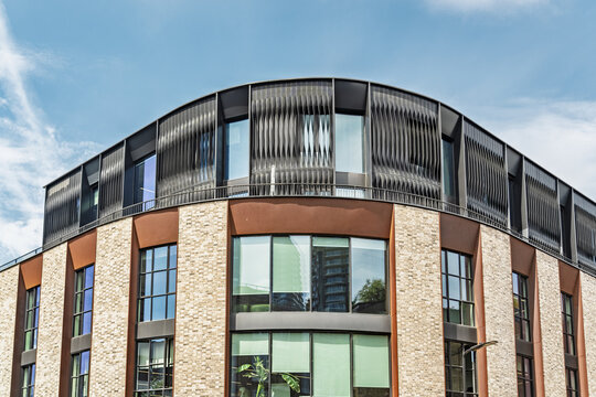 View of the modern facade of a building near Liverpool Street Station with brickwork, large windows, and a curved metallic upper level under a blue sky in London, England, United Kingdom.