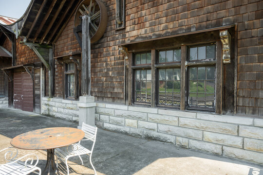 View of the historic wooden depot building with stone foundation, weathered shingles, and a rustic metal table with chairs on the concrete platform in Cedar Hill, Missouri, United States.