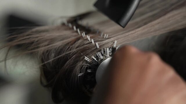 Professional hair stylist using a hot blow dryer and round brush on a female client.