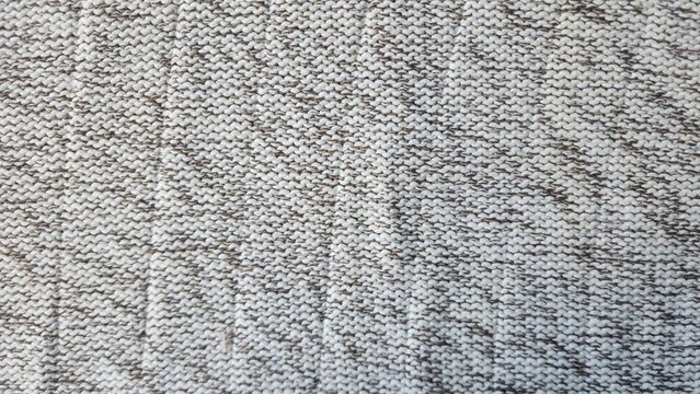 Close up of a textured knitted fabric with a marled pattern of white and dark grey threads