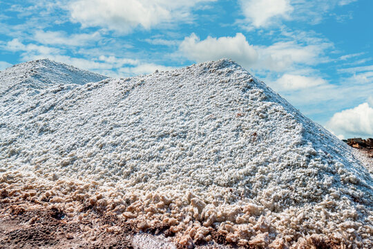 Large pile of harvested sea salt under blue sky with clouds, natural sodium chloride mineral for food manufacturing, industrial processing, organic seasoning production and raw material storage.