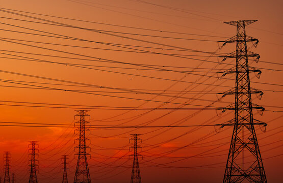 High voltage electricity transmission towers and power lines silhouetted against sunset sky. Electrical grid infrastructure, energy distribution, utility engineering and modern power networks.