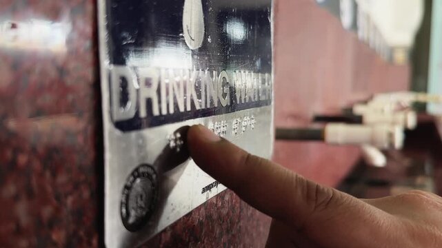 Closeup of a person touching Braille on a drinking water sign highlighting accessibility features for visually impaired individuals
