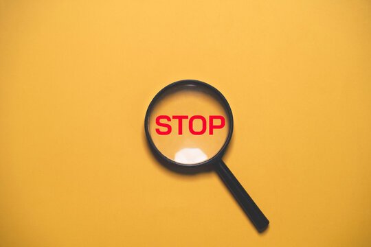 Magnifying glass highlights red STOP text symbolizing warning, restriction, risk prevention, safety caution, problem detection, prohibited action, inspection and decision making with copy space.
