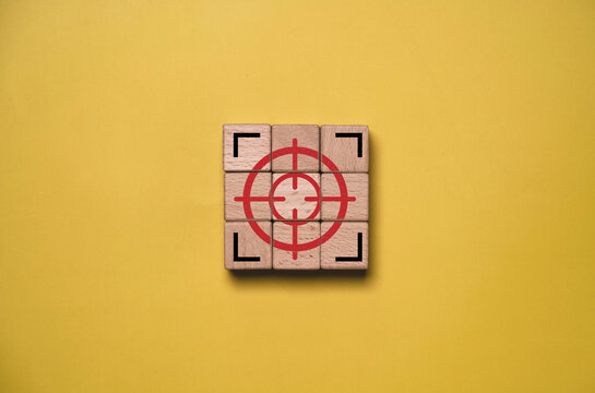 Red target crosshair on wooden blocks symbolizes business focus, goal setting, precision, strategy, objective, targeting, success, achievement and clear direction on yellow background with copy space.