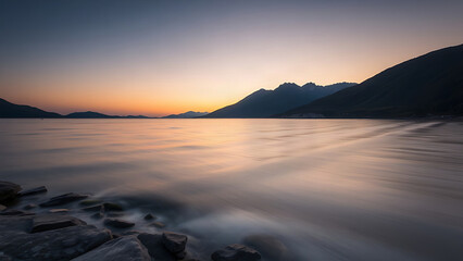 Fototapeta premium A serene mountain lake at dusk with water lapping against a stone embankment.