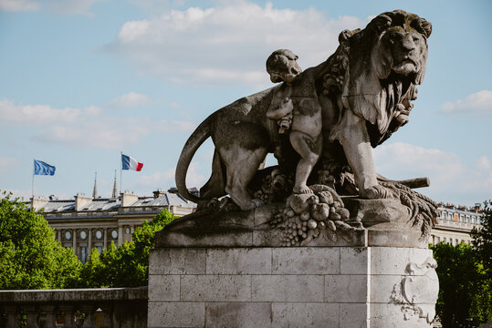 Paris, Ile-de-France, France - 06 May 2022: View of the ornate stone lion sculpture on the Pont Alexandre III bridge featuring a cherub figure and fruit carvings under a blue sky.