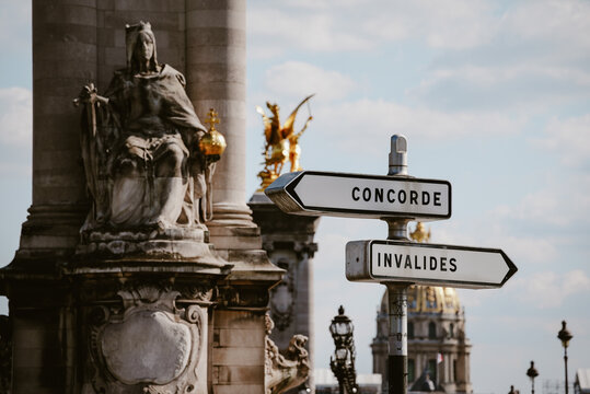 Paris, France - 06 May 2022: View of a street sign pointing towards Concorde and Invalides, with the Pont Alexandre III statue and the golden dome of Les Invalides in the background.