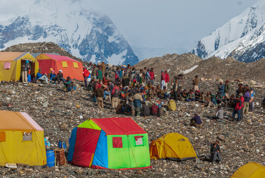 Karakoram Mountain Range, Gilgit Baltistan, Pakistan - 15 June 2007: View of Concordia base camp with colorful tents and porters gathered before the towering K2 mountain.