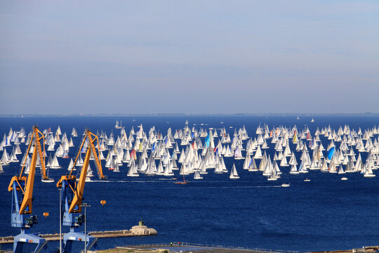 Trieste, Italy - 10 October 2010: View of the Barcolana Regatta with numerous sailboats on the blue sea, framed by large industrial cranes in the foreground.