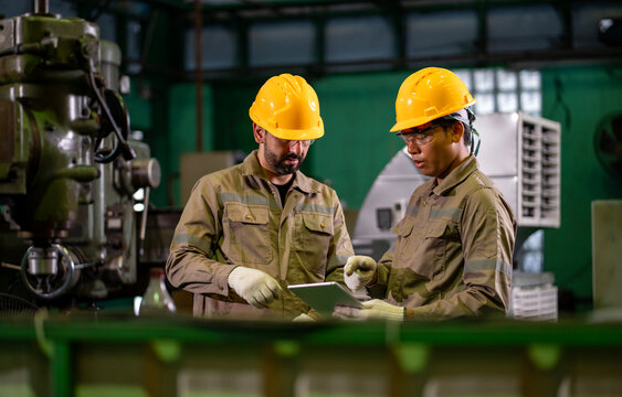 Team of industrial worker is checking the setup value of  metal casting machine by automated monitor while working inside roof factory for safety industry