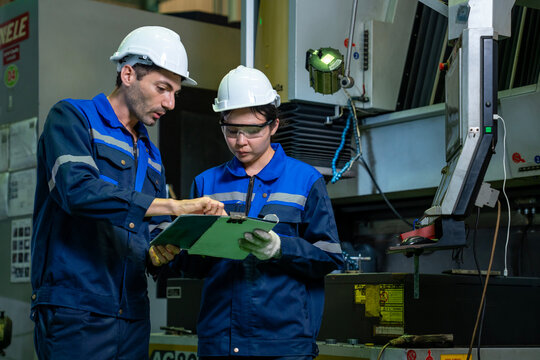Team of industrial worker is checking the setup value of  metal casting machine by automated monitor while working inside roof factory for safety industry