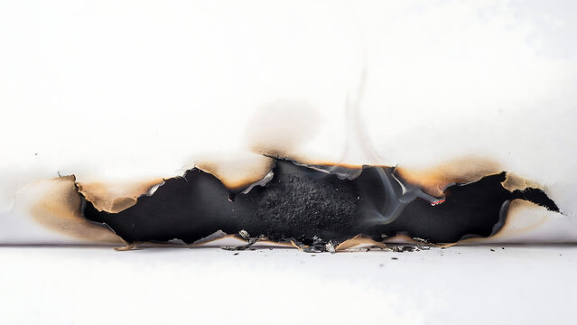Closeup of a burnt hole in a white paper sheet with smoke rising, isolated on white background