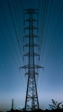 Perfectly symmetrical vertical view of a high voltage transmission tower silhouette against a cinematic starry night sky with a deep blue gradient.