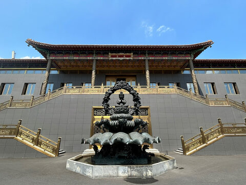 Leshan, Sichuan, China - 08 August 2026: View of the Jinding Golden Summit temple with golden railings, dark stone facade, and a bronze deity statue on a lotus base under a clear blue sky.