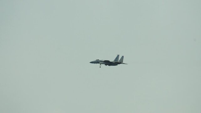 A military F-15 fighter jet flies through the sky on landing approach.