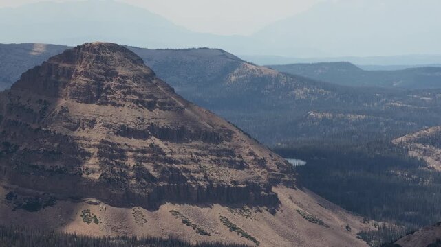 Aerial of rugged mountain landscape in Uinta Wasatch Cache National Forest Utah with prominent arid peaks and cliffs transitioning into dense evergreen forests and small lakes in summer