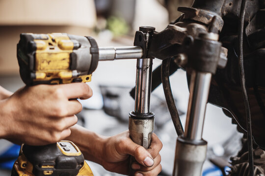 Mechanic using cordless impact wrench to disassemble motorcycle front fork and triple tree assembly