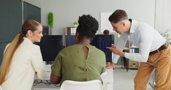 Programmers developers team coding collaboration at office. Teammates review code on dual screens as a mentor guides problem solving. Clear concept of collaborative software development teamwork.