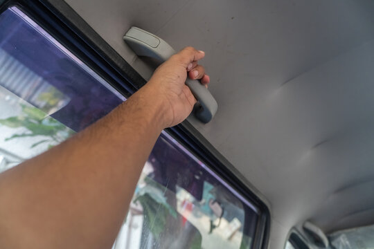 Close up of a person hand holding a ceiling grab handle inside a car for safety, travel support, and commuter vehicle interior mechanics.