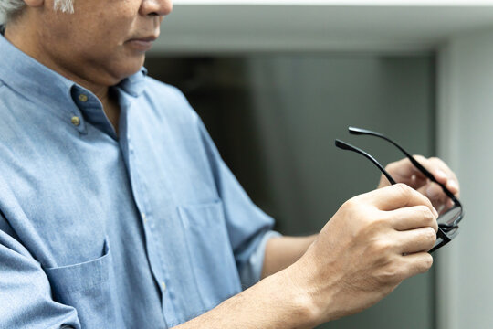 Asian elderly senior man with eyesight issue, concept image of aging eye sight, vision deterioration, elderly vision problem, hand holding eyeglasses closeup shot, home indoor scene