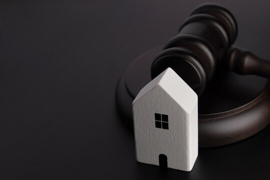 Miniature house and a judge's gavel on a black background with copy space for text. Real estate law, property foreclosure, auction, eviction concept.