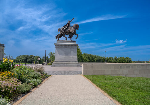 St. Louis, United States - 07 August 2026: View of the Saint Louis statue in Forest Park, featuring the bronze equestrian monument set against a clear blue sky with surrounding flower beds.