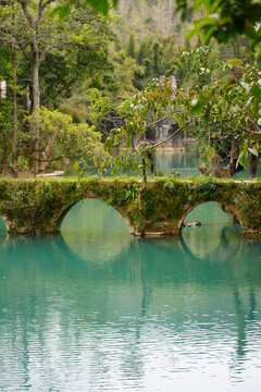 Mossy Stone Arch Bridge over Turquoise Water in Xiaoqikong Scenic Area, Guizhou, China