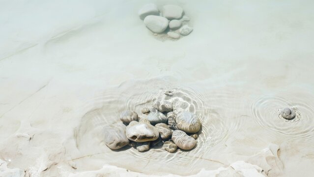Smooth grey pebbles submerged in shallow clear water, ripples
