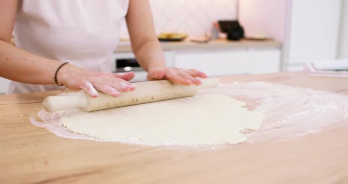 Bakery process. Pastry recipe. Female confectioner hand rolling dough sheet with kitchen pin on flour home countertop making dessert.