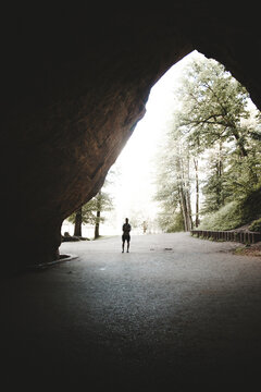 Sigulda, Latvia - 25 July 2023: View of a person standing inside the entrance of the historic Gutmanis Cave with lush forest surroundings.
