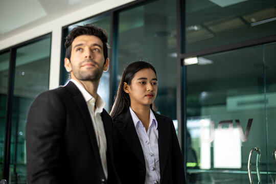 Business professionals man and woman in office wearing formal suits, standing together with focused expressions, workplace teamwork, corporate career, leadership and planning