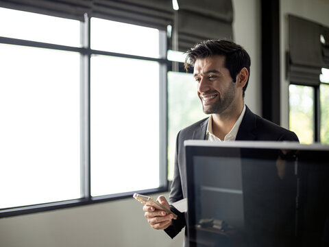 Smiling business man using smartphone at modern office reception, professional corporate traveler showing confidence, communication, technology, workplace and customer service