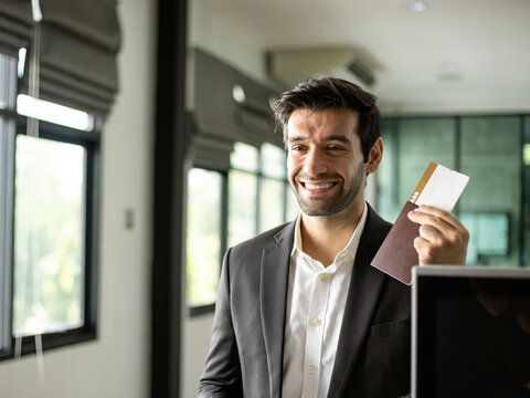 Smiling business traveler holding passport and boarding pass at office reception, showing travel documents, confidence, corporate trip, checkin and professional mobility