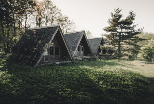 Merikula, Harju maakond, Estonia - 19 May 2023: View of abandoned A-frame cabins nestled in a forest clearing with overgrown grass and tall trees.