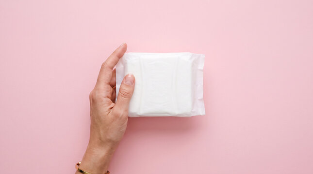 Hand holding wrapped sanitary pad on pink. Minimalist concept for menstrual health and hygiene.