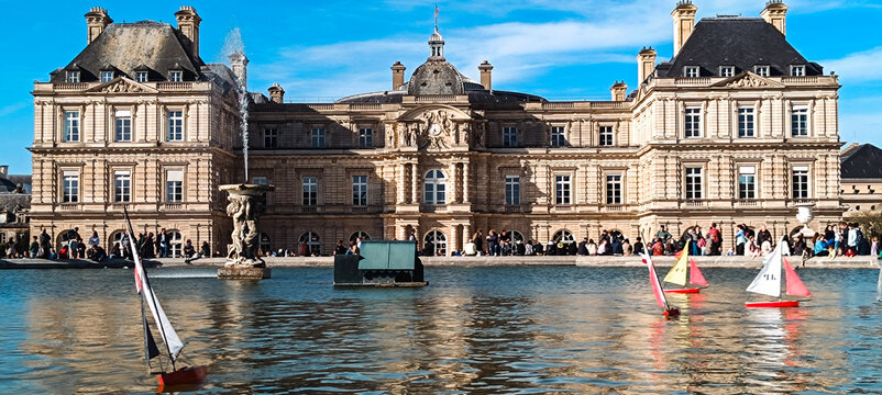 Paris, France - 04 April 2026: View of the Luxembourg Palace with its iconic fountain and toy sailboats on the water, surrounded by people enjoying a sunny day in the park.