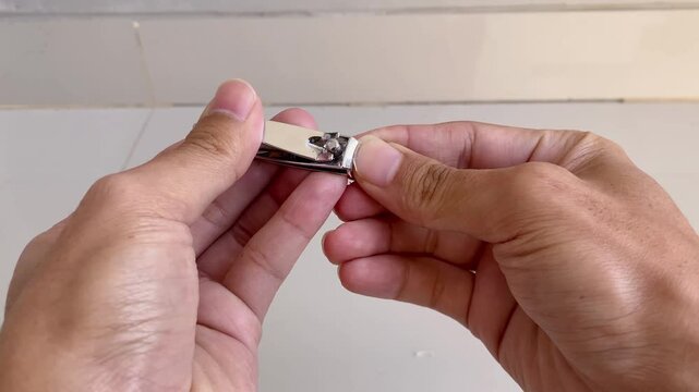 A close up view of a person using a metal nail clipper to trim their fingernails for personal grooming and hygiene.